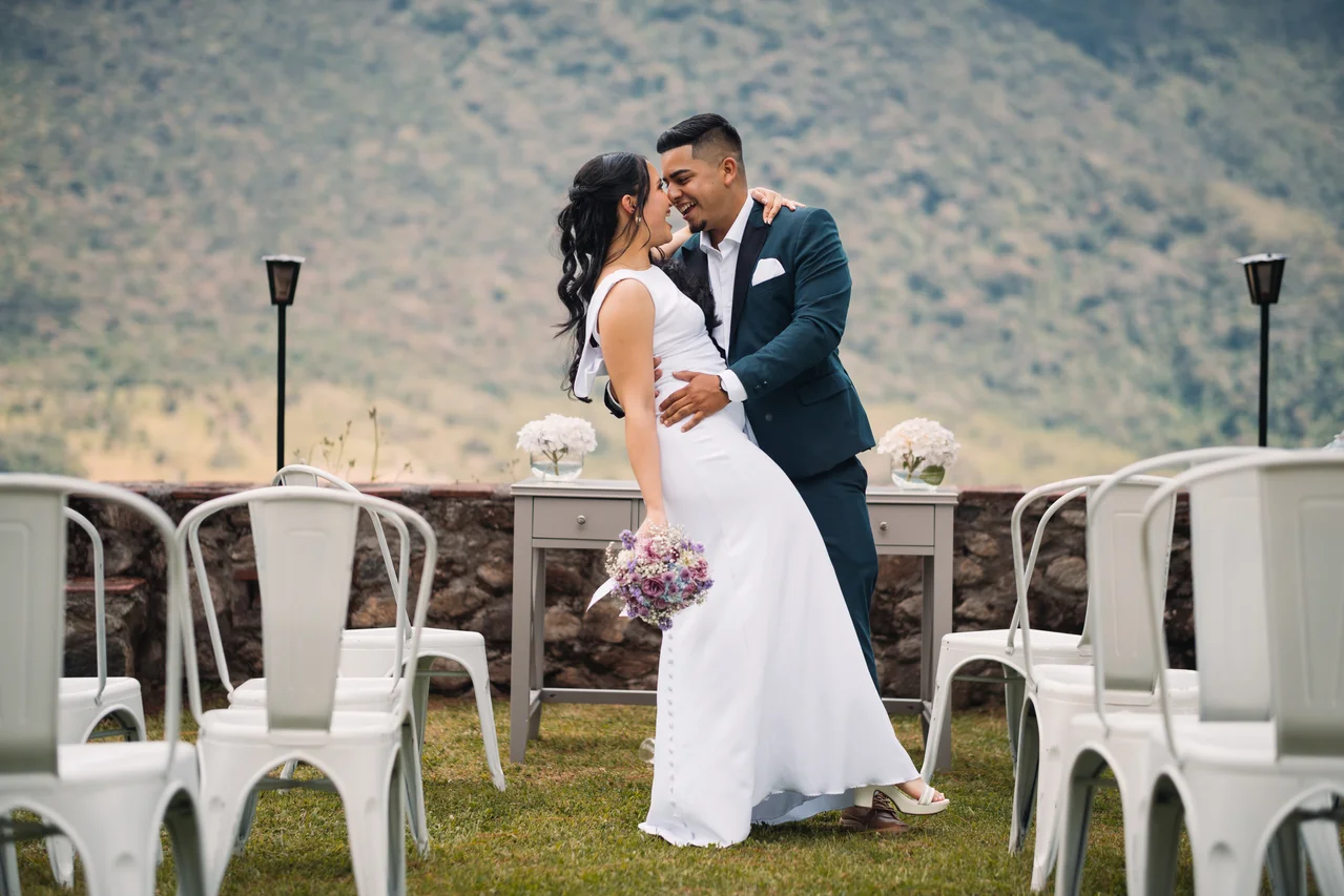 Novios riendo entre las sillas de la ceremonia con montaña al fondo