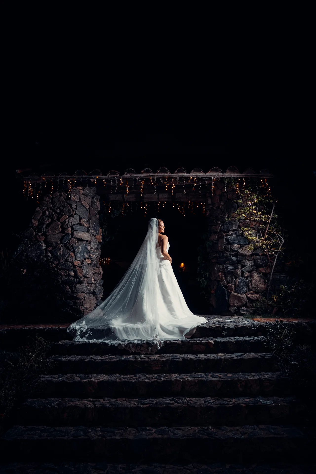 Novia y velo iluminados de noche en escalones de piedra, rodeados de sombra