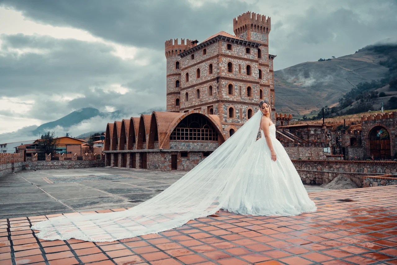 Novia y largo velo sobre patio de ladrillo, castillo y montañas con nubes