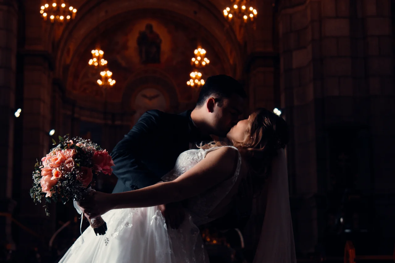 Beso de pareja dentro de la iglesia con luz cálida y fondo oscuro
