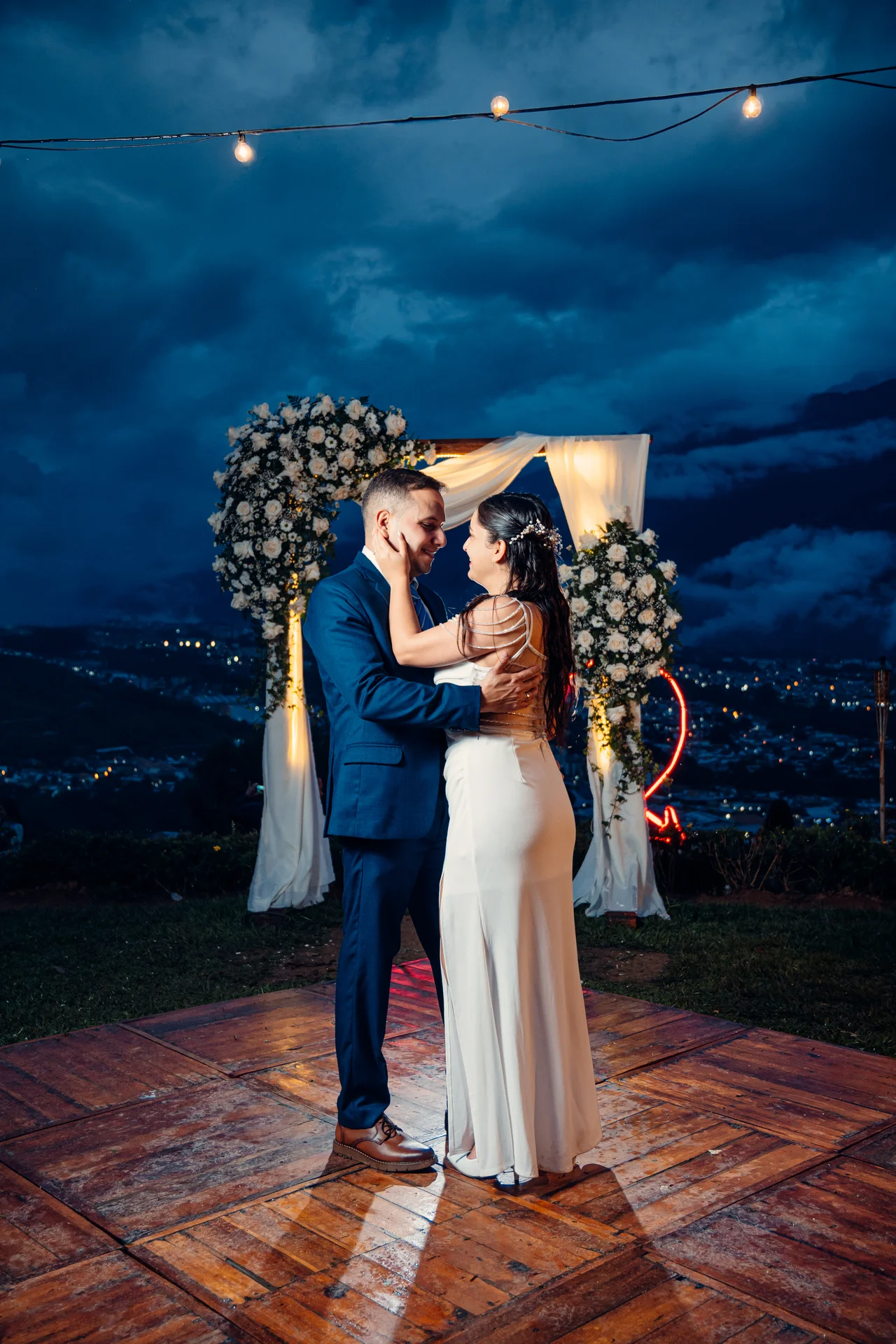 Pareja bajo arco iluminado al caer la tarde, cielo azul y montañas nubladas
