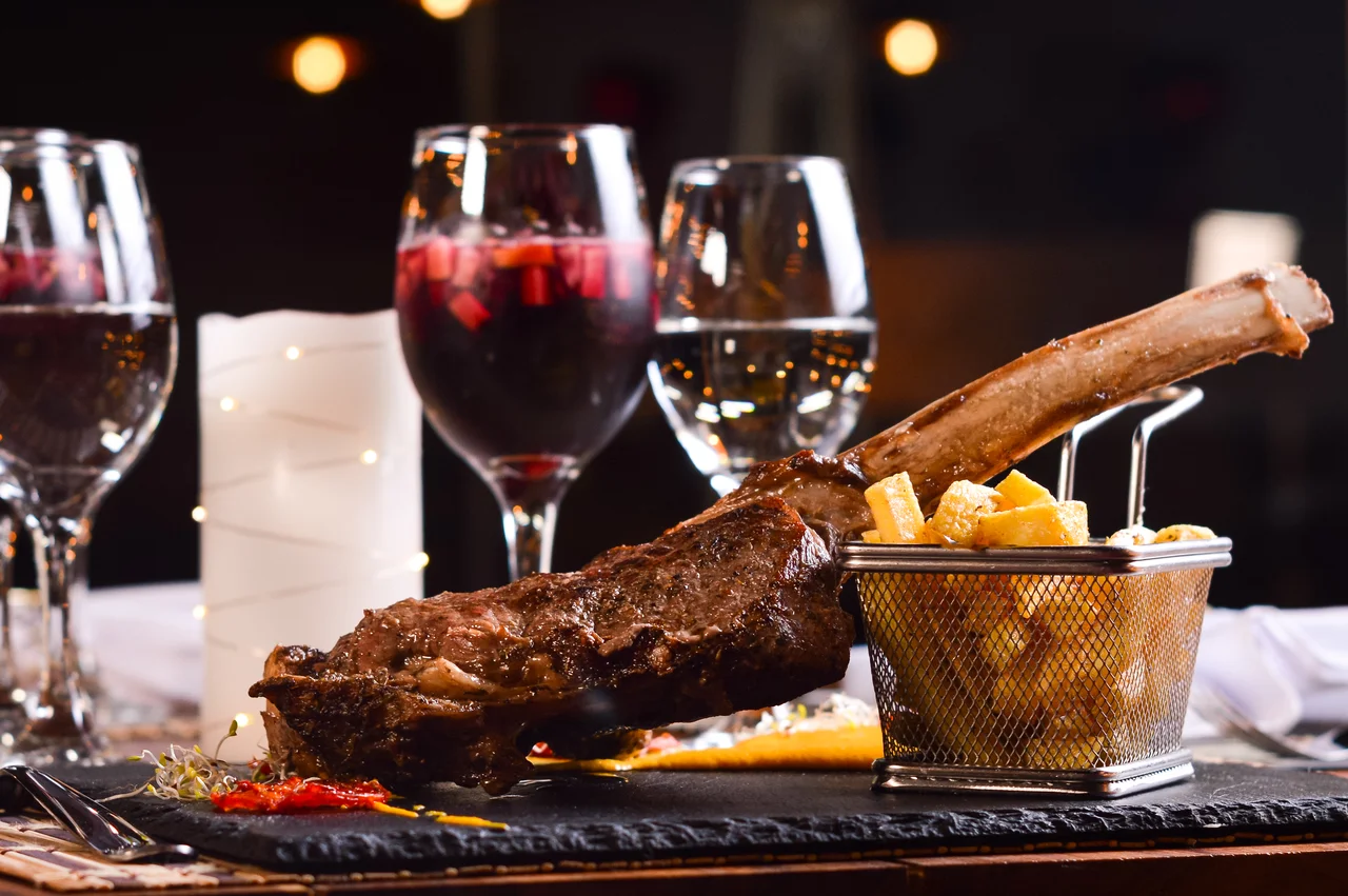 Tomahawk con papas, copas y ambiente de restaurante