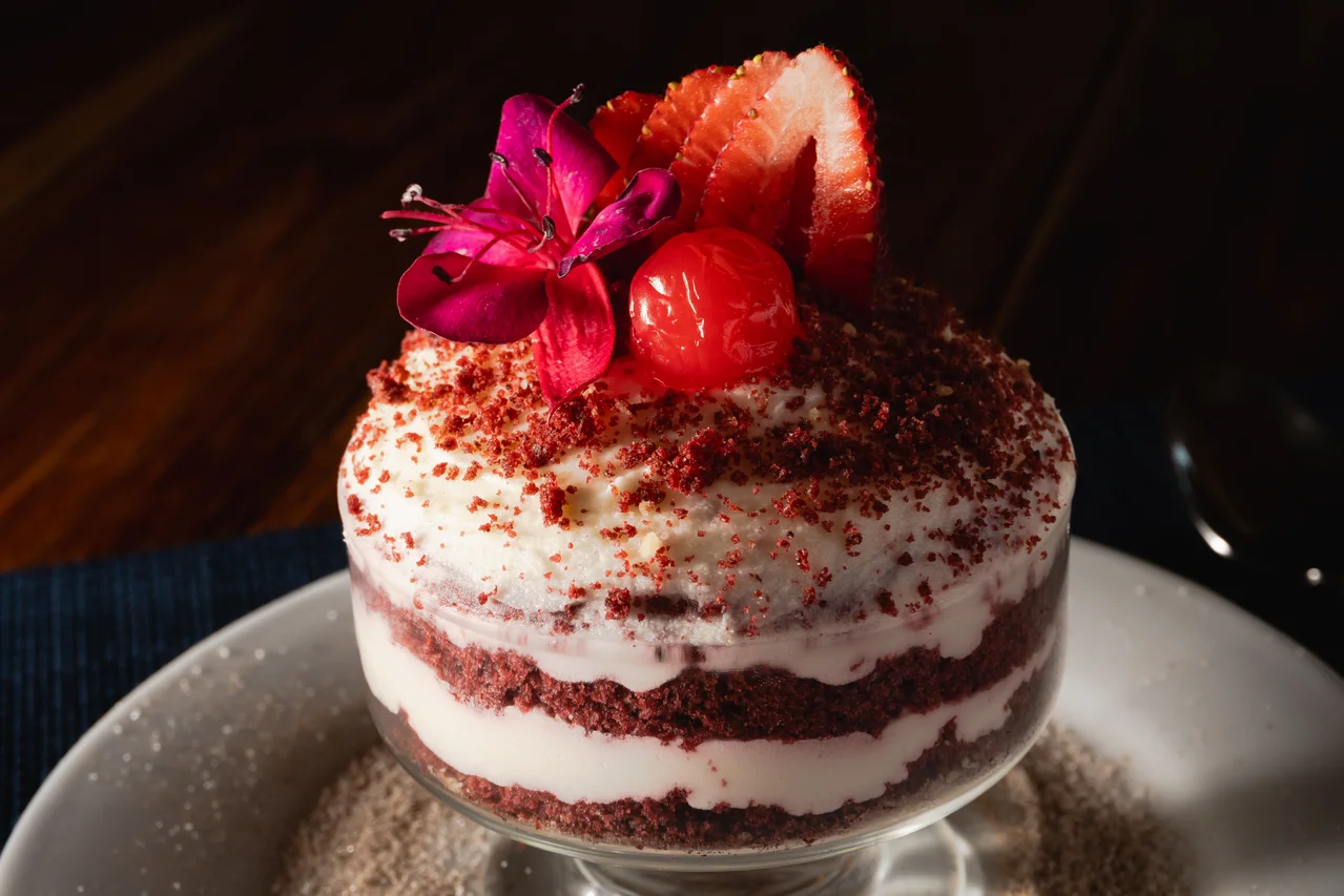 Pastel individual de capas rojas y crema, con decoración de fruta y flor roja