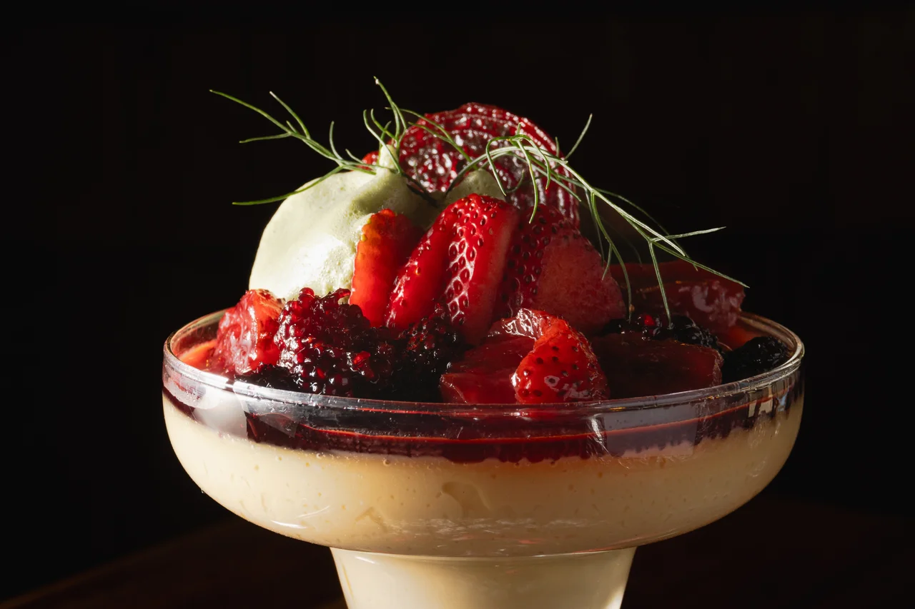 Detalle de postre en copa con frutos rojos y crema sobre fondo oscuro