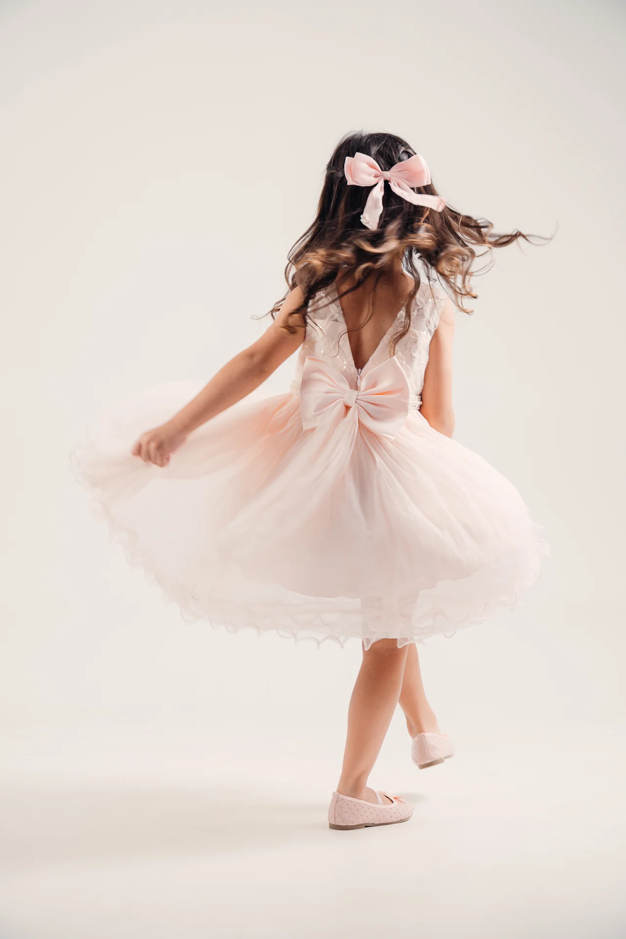 Vestido infantil rosa en giro, cabello y falda en movimiento contra fondo marfil