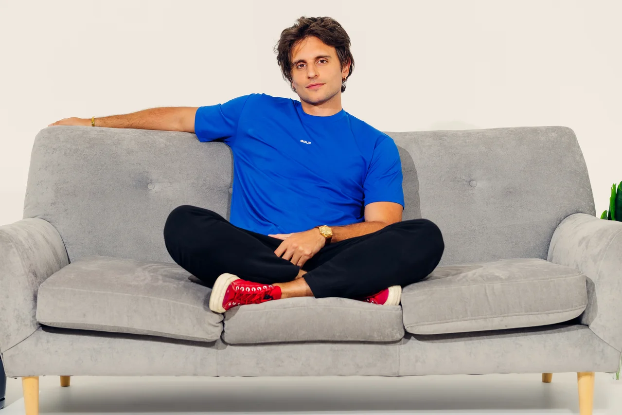 Campaña GOUP con modelo de camiseta azul y zapatos rojos sentado en sofá gris