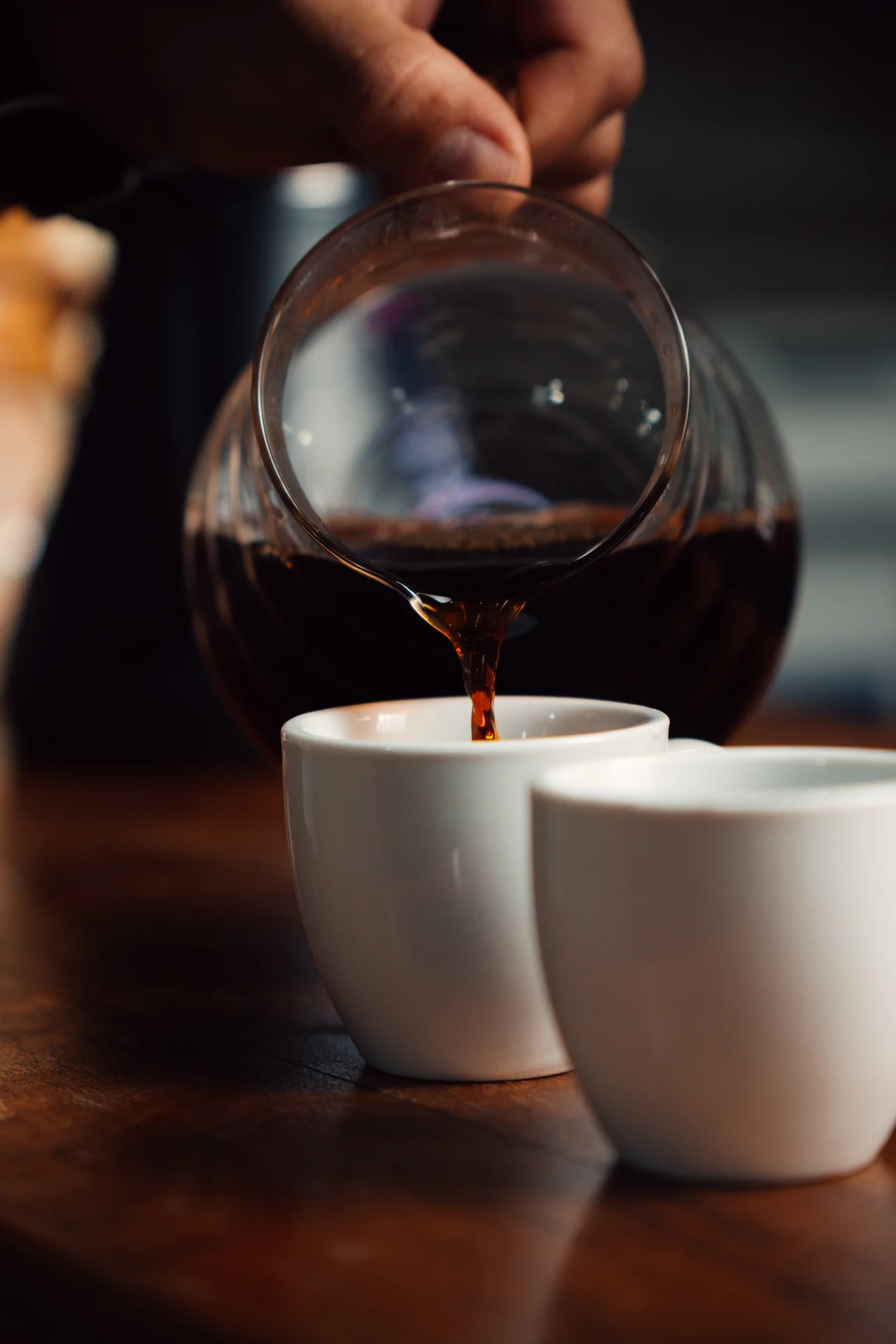 Café vertiéndose desde jarra de cristal a taza blanca