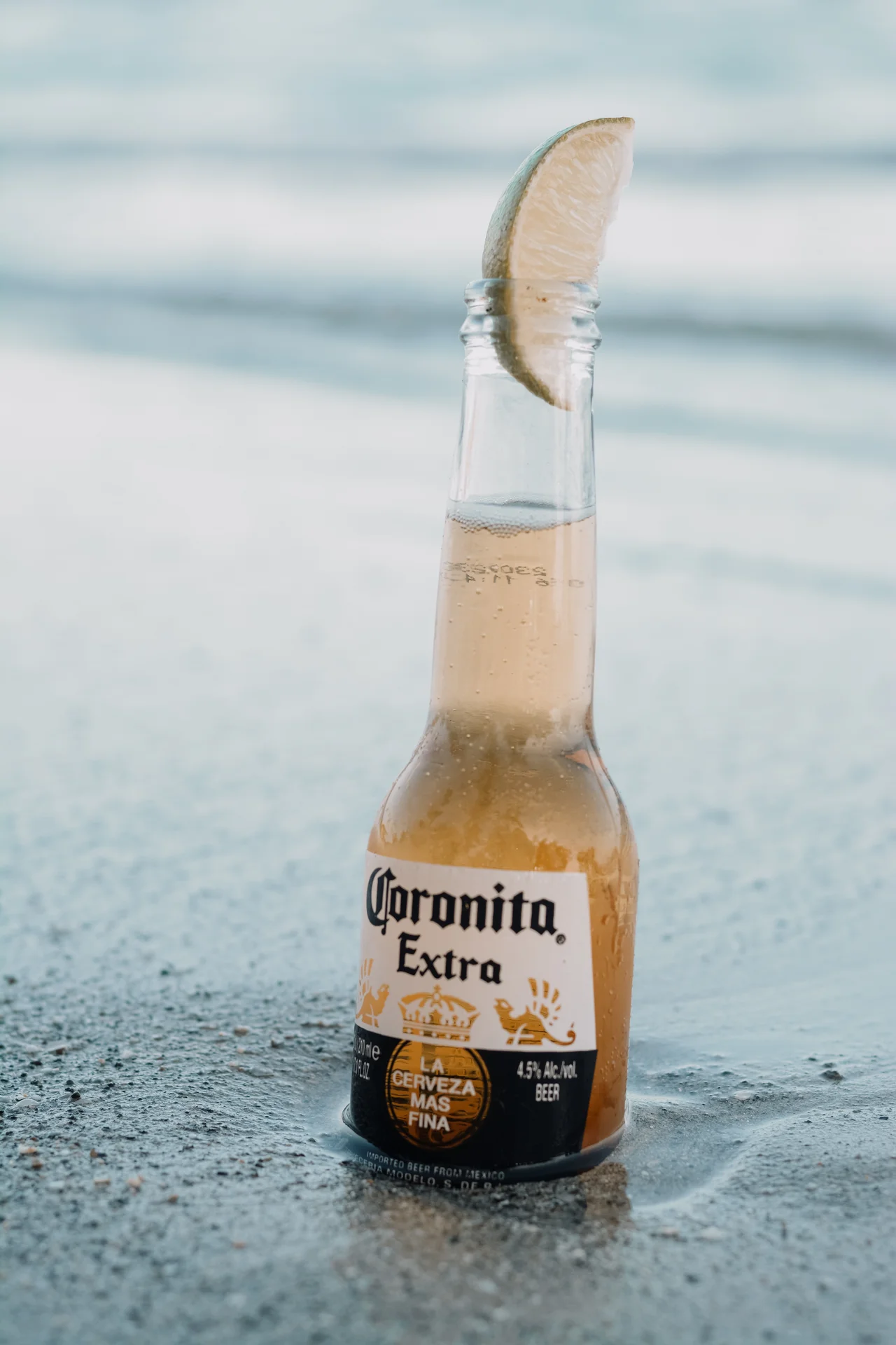 Coronita con limón sobre arena y mar desenfocado