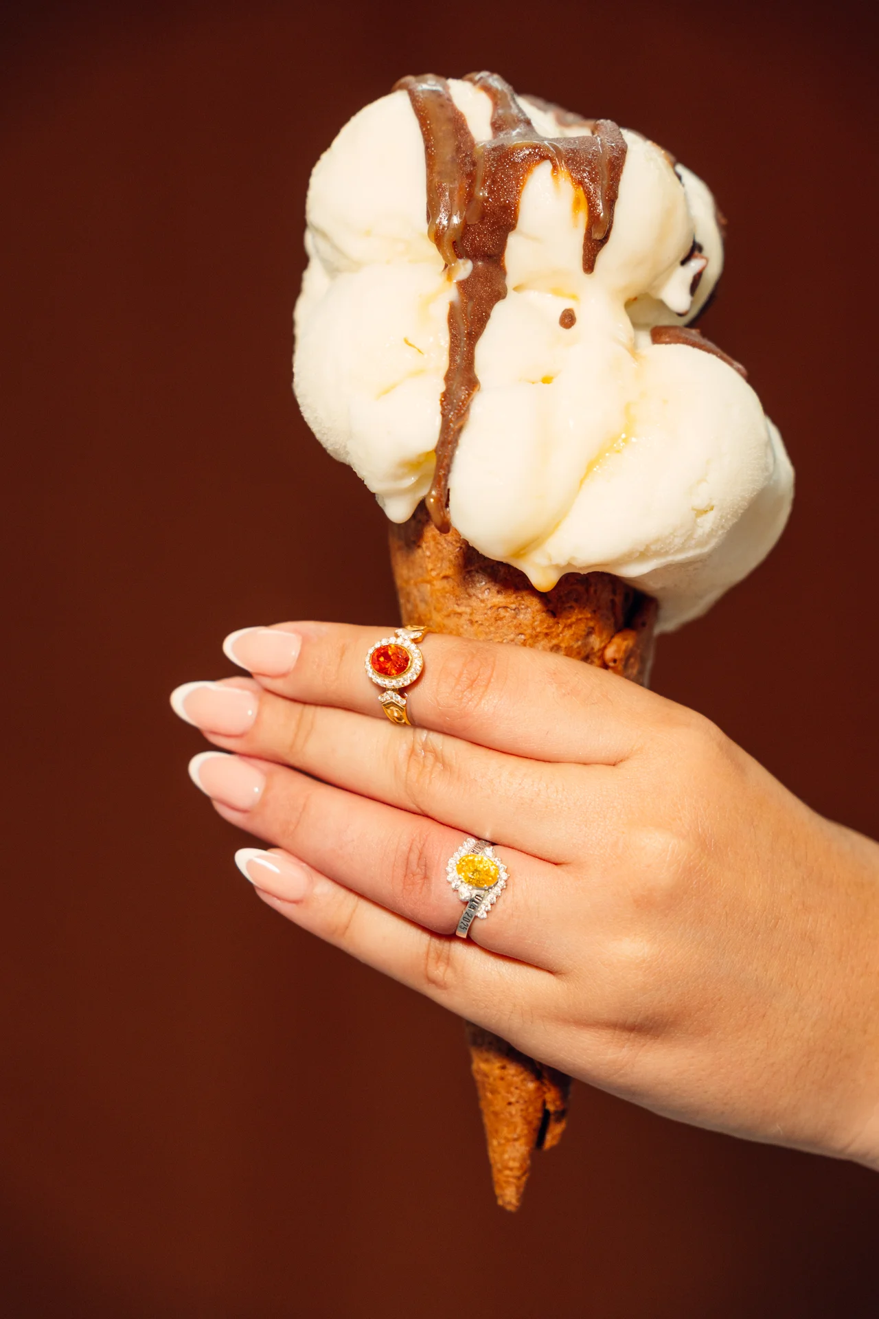 Anillos de colores en una mano que sostiene un helado sobre fondo cálido