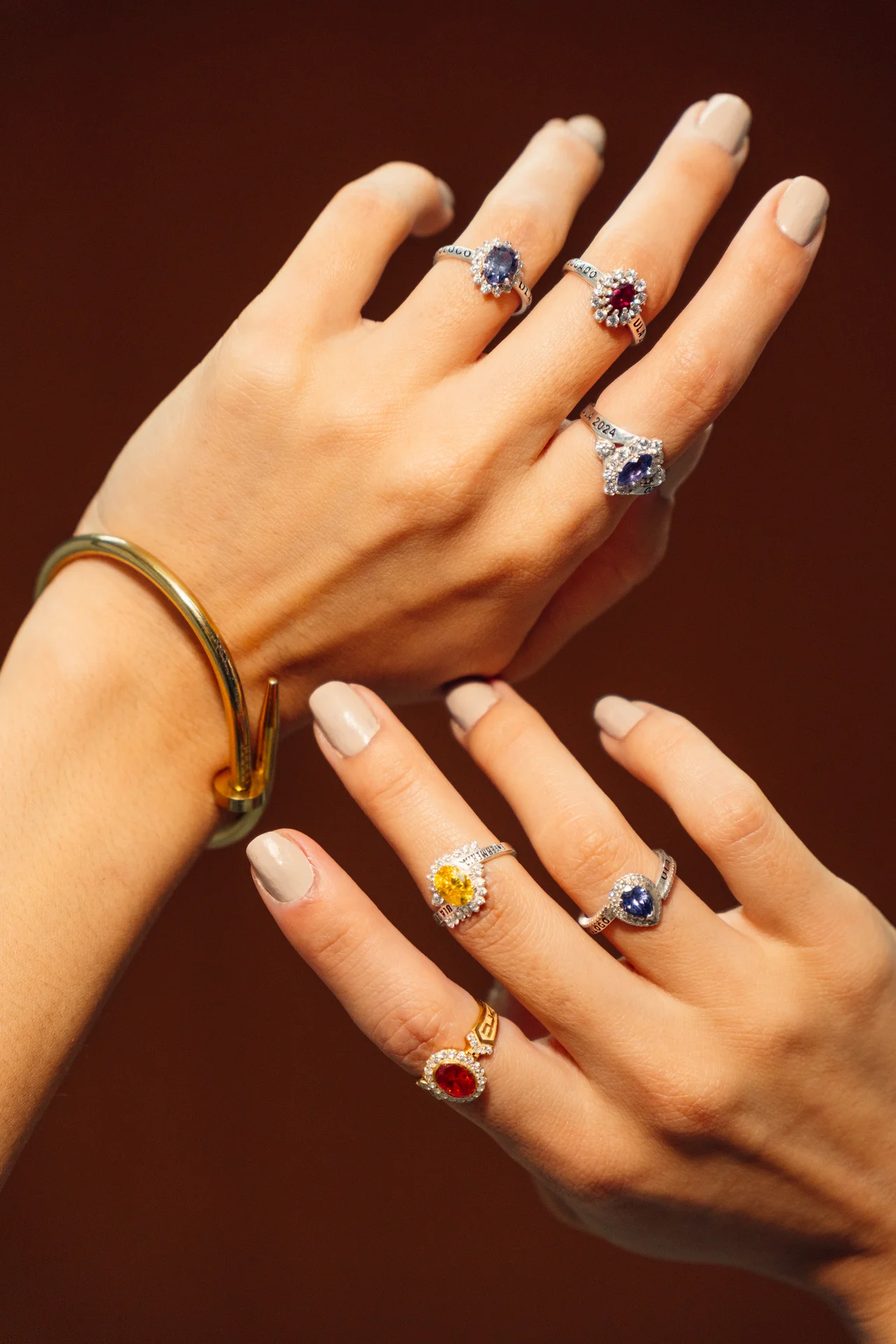 Dos manos con anillos de piedras de colores sobre fondo terracota