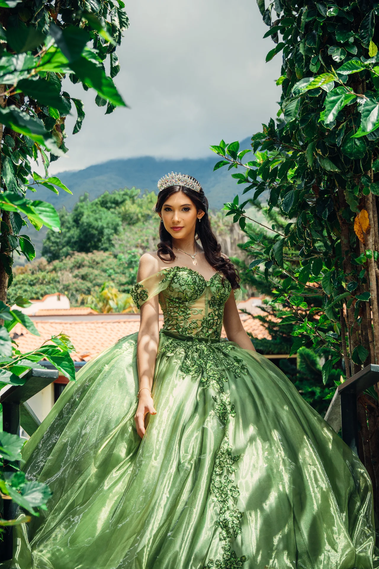 Retrato de quinceañera enmarcada por vegetación con vestido verde y montañas al fondo