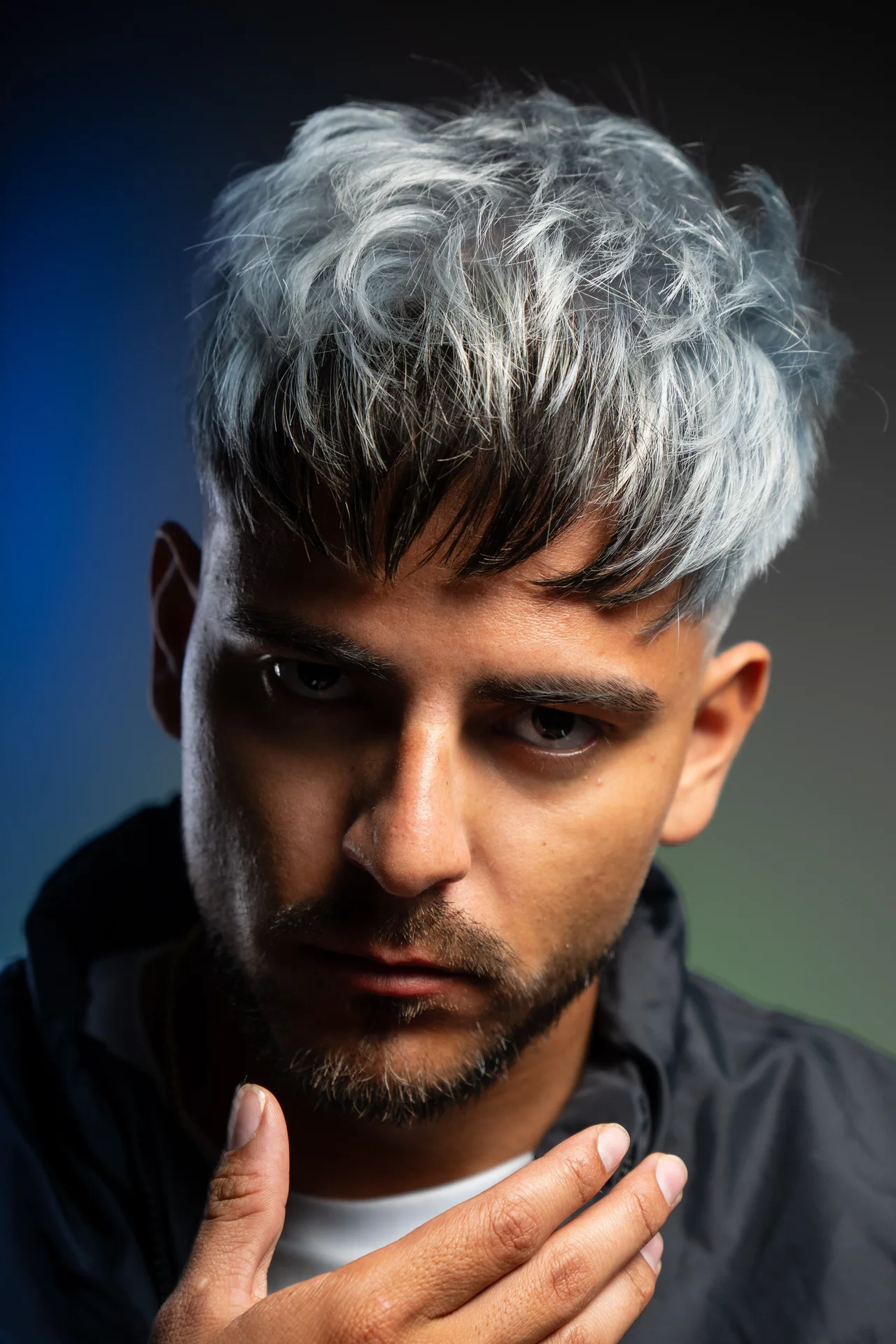 Retrato masculino cerrado con pelo gris, mirada intensa y luz lateral sobre fondo azul
