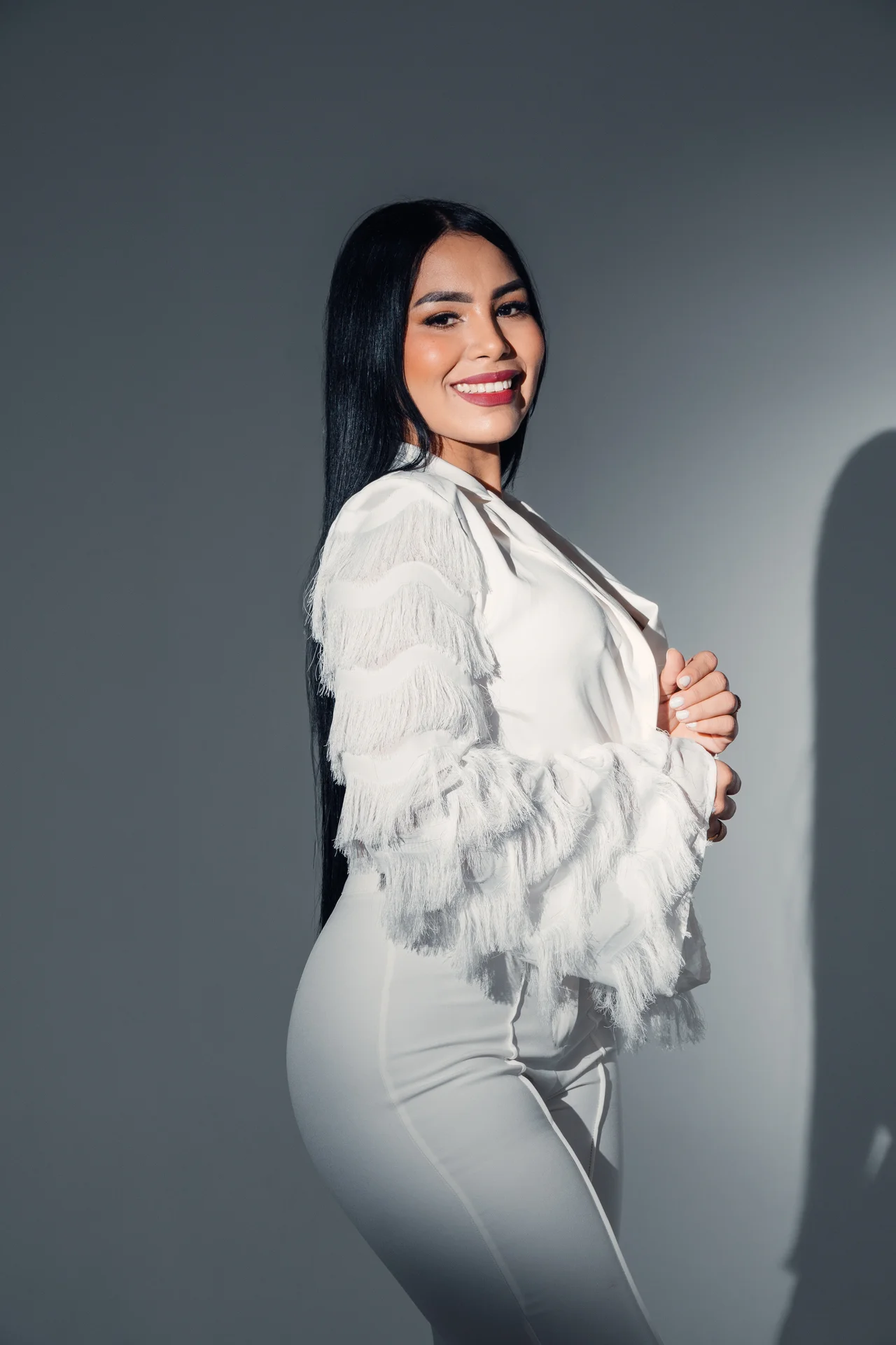Retrato editorial con traje blanco de flecos y luz recortada sobre gris