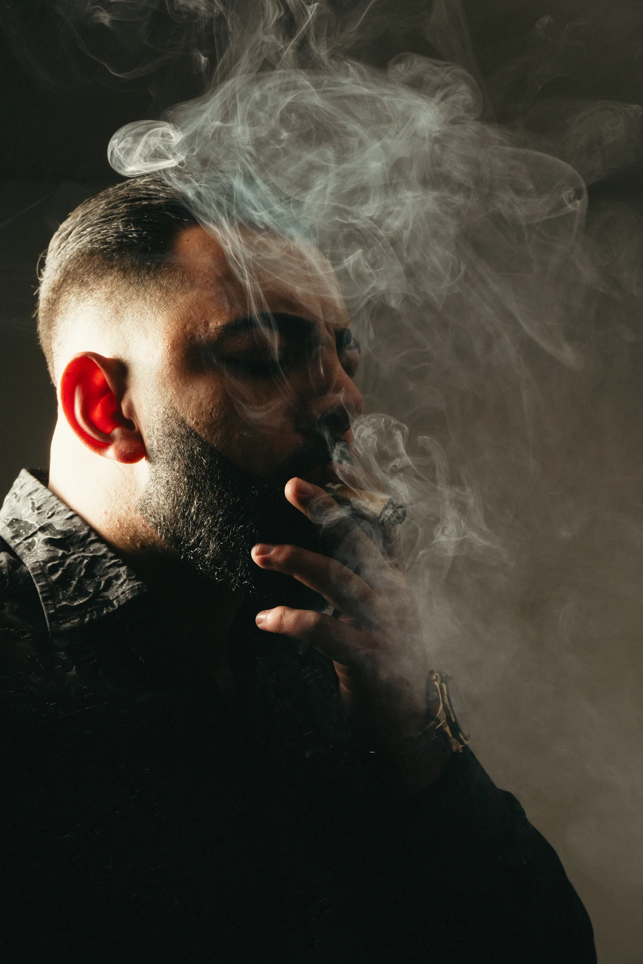 Retrato dramático lateral con humo del puro dibujado por contraluz y fondo neutro